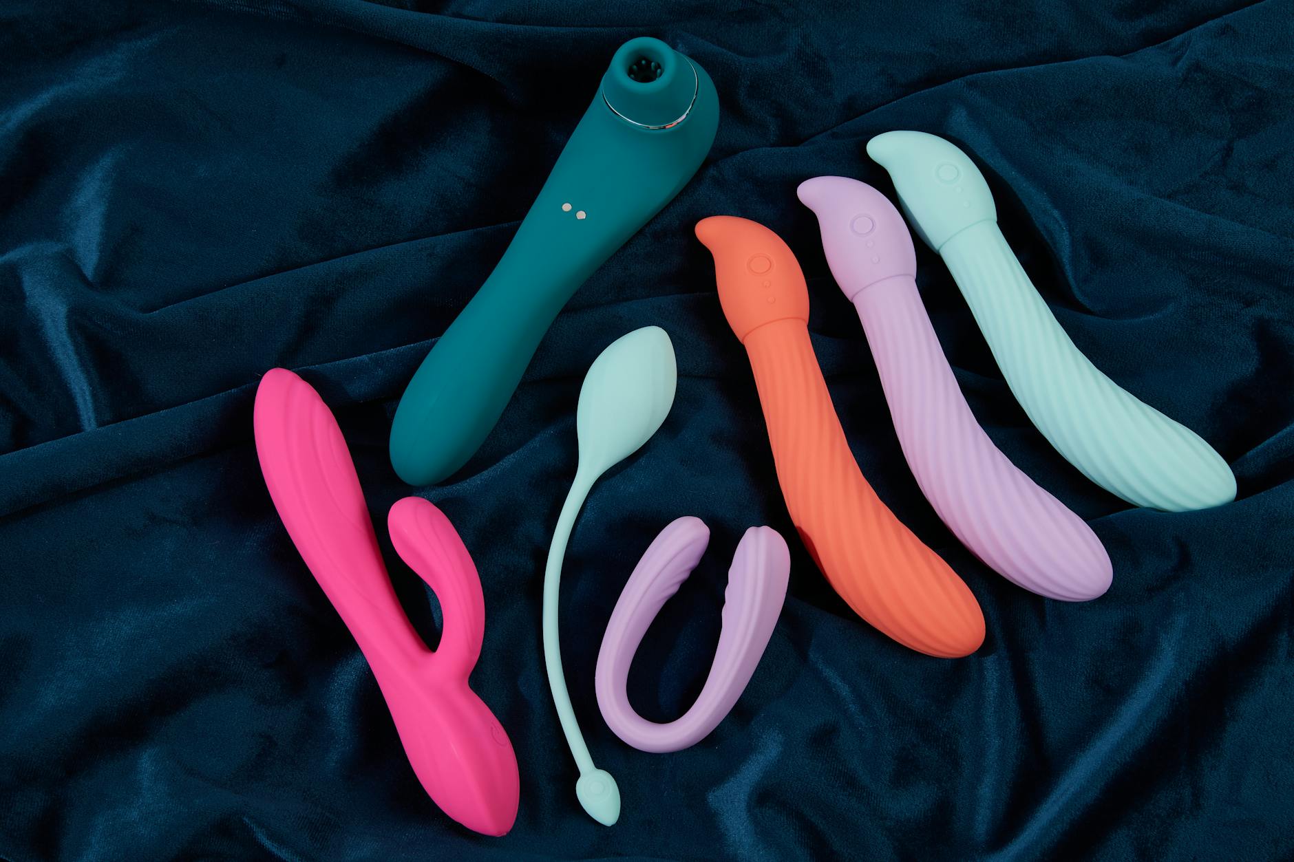 Blue silicone clitoral vibrator held in hand against purple background