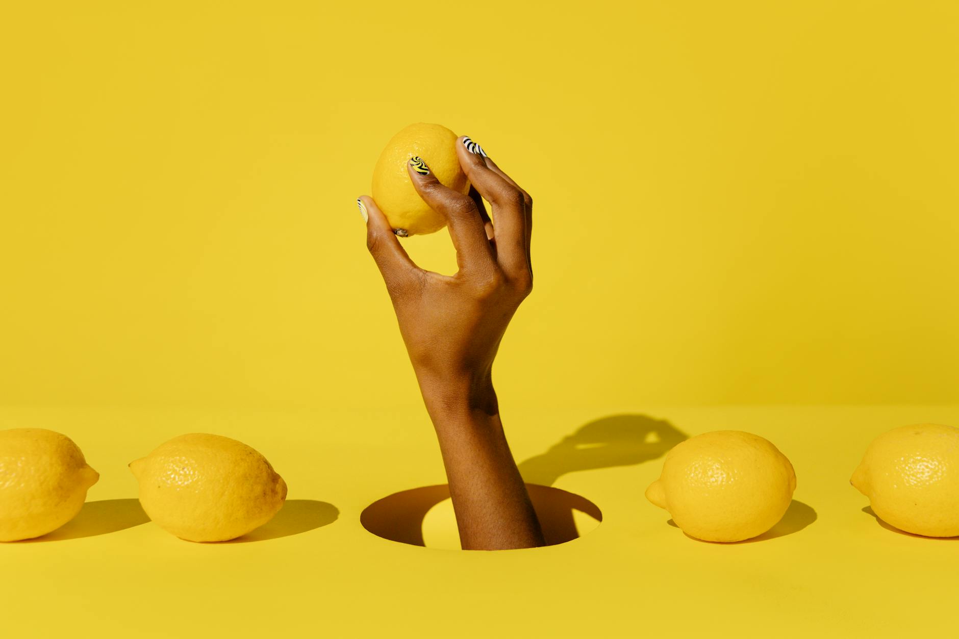 A hand holding a fresh lemon against a vibrant yellow background, representing the sensation-focused approach to pleasure