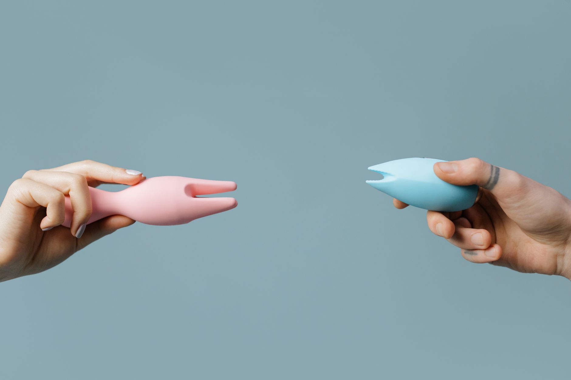 Two people holding colorful vibrators against a pastel background, representing shared pleasure and partnership.