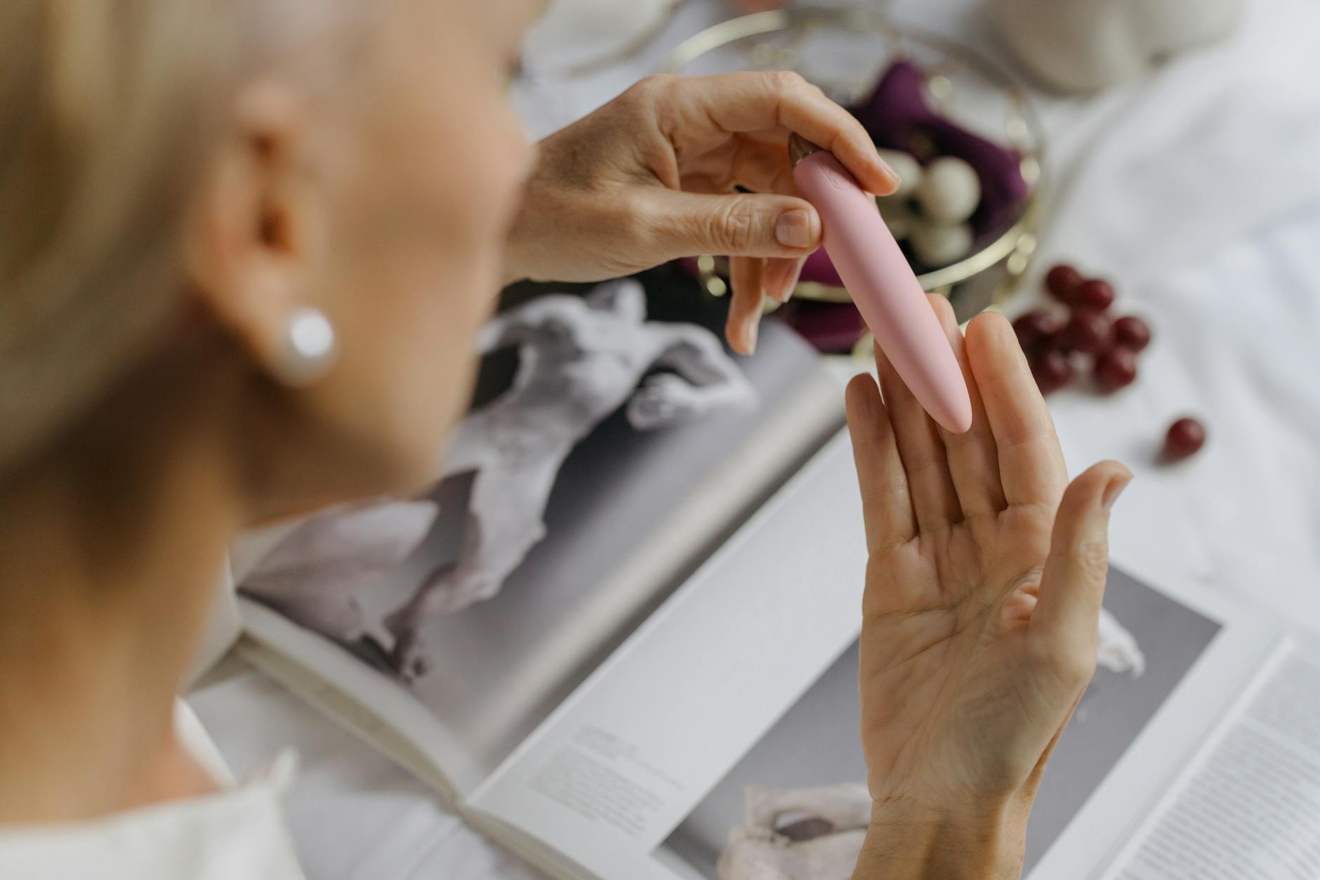 Woman holding a pink vibrator, with art books in the background