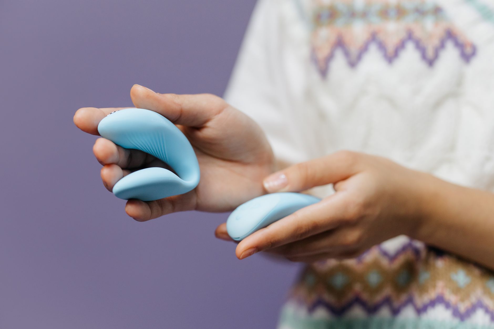 Hands holding a sleek blue vibrator against a purple background.