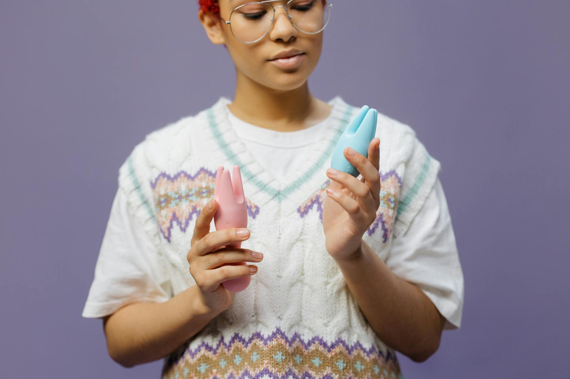 Person holding blue and pink silicone vibrators, considering options for clitoral sensitivity